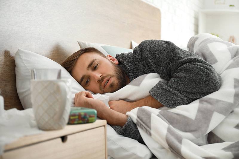 Mann mit Erkaltung liegt im Bett